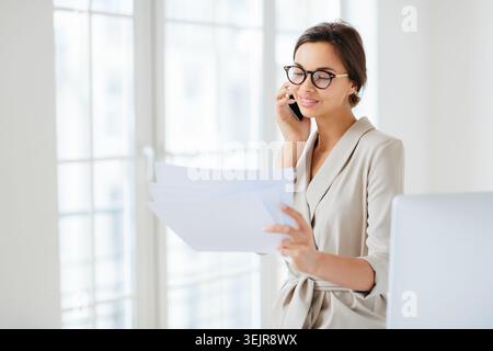 Femme d'affaires parlant au téléphone et lisant des documents au bureau Banque D'Images