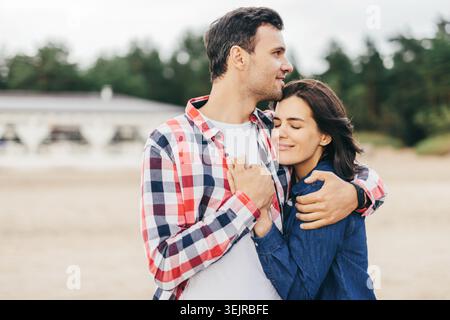 Jeune couple embrassant sur la plage en plein air partage moment romantique près de fond de forêt Banque D'Images
