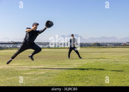 Hommes matures jouant au baseball, sautant et regardant sur terrain herbeux avec des gants, espace de copie. Athlètes, terrain, extérieur, ensoleillé, Banque D'Images