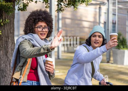 Diverses amies féminines marchant dans la place urbaine signalant la palme, tenant le café et tirant la valise. Femmes, bagages, sac à dos, gla Banque D'Images