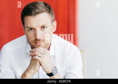 Portrait d'homme sérieux en chemise blanche avec les mains sous le menton pour photo de profil professionnel Banque D'Images