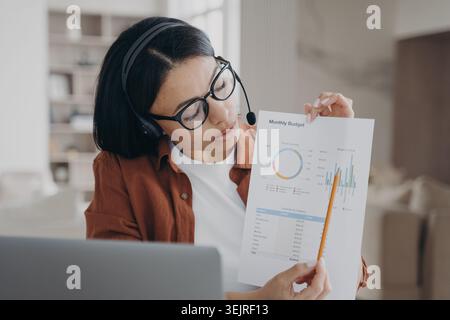 Jeune femme asiatique portant casque présente le graphique de budget mensuel pendant la réunion d'affaires en ligne Banque D'Images