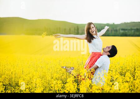 Heureux jeune couple jouant dans le champ de colza jaune pendant la marche de campagne de printemps Banque D'Images