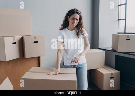 Une jeune femme stressée emballe des boîtes en mouvement dans un appartement lumineux près de la fenêtre Banque D'Images