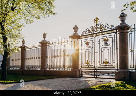 Porte en fer forgé ornée avec piliers en pierre et lumière du soleil dorée dans l'entrée formelle du parc Banque D'Images