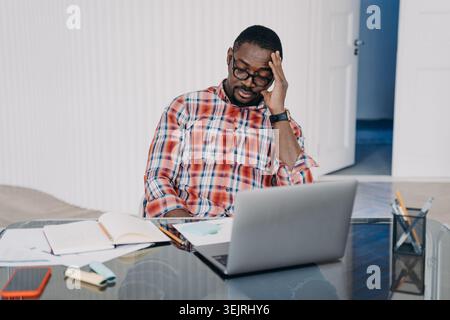 Homme stressé regardant l'ordinateur portable tout en travaillant au bureau dans le bureau à domicile Banque D'Images