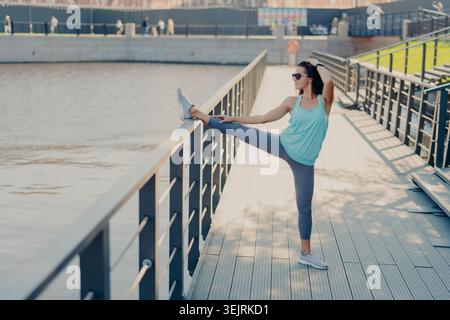 Fit jeune femme dans Sportswear Stretching Leg High sur la rampe en métal sur Riverside Promenade pendant l'entraînement matinal en plein air Banque D'Images