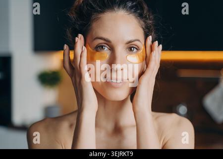 Jeune femme appliquant sous les patchs oculaires pendant la routine de soin de la peau à la maison Banque D'Images