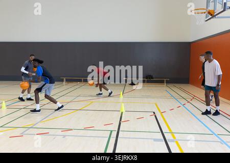 Divers joueurs masculins portant des vêtements de sport pratiquant dribble sur un terrain de bois franc avec des balles et des cônes. Basketball, gymnase, floo Banque D'Images