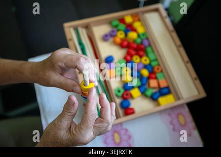 Vue rapprochée des mains froissées d'une personne âgée pratiquant une ergothérapie cognitive et motrice en glissant des perles de bois multicolores Banque D'Images