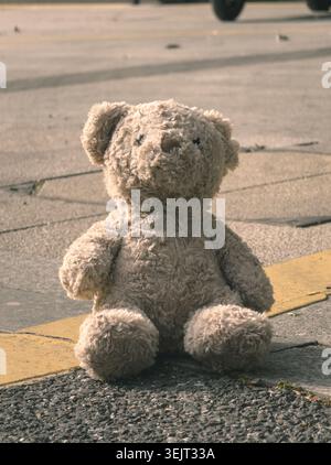 Lost Furry Teddy Bear est assis oublié sur une rue asphaltée texturée à côté d'une route jaune vif marquage en plein soleil Banque D'Images