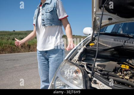 Femme en auto-stop près de sa voiture en panne sur la route Banque D'Images