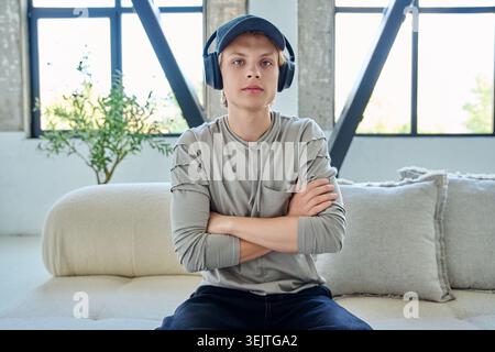 Jeune homme en casquette et écouteurs assis sur le canapé Banque D'Images