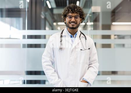 Jeune médecin masculin debout confiant et souriant, portant une blouse de laboratoire et un stéthoscope, représentant la santé, la médecine et le bien-être dans un environnement médical moderne Banque D'Images