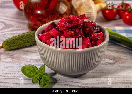 Salade traditionnelle de betteraves avec des légumes coupés en dés dans un bol gris sur fond de bois rustique. Plat magenta vibrant entouré d'ail frais, de cornichons, elle Banque D'Images