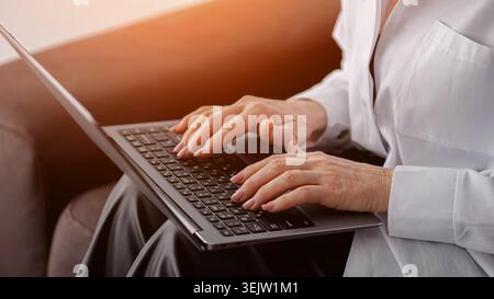 Les mains des femmes sont occupées à taper sur un clavier d'ordinateur portable, engagées dans le travail à distance ou la communication en ligne, incarnant la productivité et la connexion dans un moderne Banque D'Images