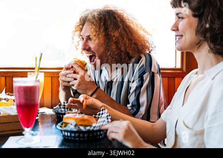 Groupe multiethnique de jeunes amis heureux se liant au restaurant vintage diner burger House - amis divers se liant autour de hamburgers et de boissons dans un CA Banque D'Images