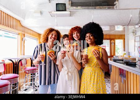 Groupe multiethnique de jeunes amis heureux se liant au restaurant vintage diner burger House - groupe de jeunes amis heureux souriant et tenant de la nourriture et Banque D'Images
