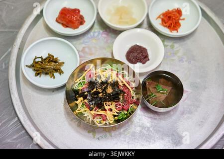 Yukhoe bibimbap propose du bœuf cru frais sur du riz et des légumes. Associé à une soupe claire de sang de bœuf et à des accompagnements, il propose un copieux repas coréen. Banque D'Images
