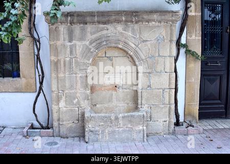 Vue au niveau de la rue d'une fontaine murale historique flanquée de vignes grimpantes sur un trottoir à Nicosie, Chypre. Banque D'Images