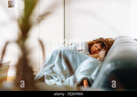 jeune femme se trouve sur un canapé en cuir recouvert d'une couverture chaude et confortable Banque D'Images