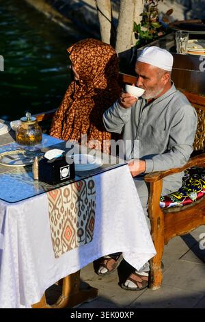 Boukhara, Ouzbékistan - 11 avril 2026 : homme ouzbek en robe traditionnelle buvant du thé sur la place Lab-i Hauz. Banque D'Images