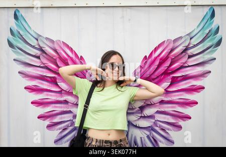 Jeune femme posant devant une murale colorée d'art de rue d'ailes d'ange Banque D'Images