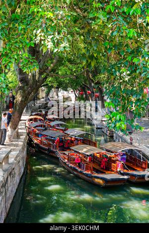 Longue file d'attente de bateaux de croisière traditionnels en bois amarrés le long d'un canal ombragé pittoresque dans la ville d'eau de Tongli, Jiangsu, Chine Banque D'Images