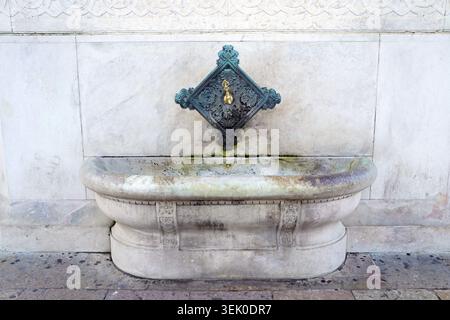 Un robinet en bronze orné est centré au-dessus d'un bassin en marbre usé sur un mur de fontaine historique avec des sculptures géométriques délicates à Istanbul, en Turquie Banque D'Images