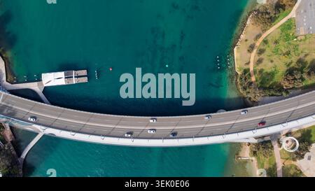 Cette superbe prise de vue aérienne capture un pont courbe moderne qui traverse une étendue d'eau turquoise vibrante, créant une vue panoramique. La photo Highl Banque D'Images