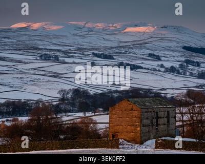 Grange en pierre dans un paysage enneigé avec des murs de pierres sèches et la lumière du soleil tôt le matin sur les collines enneigées à Wensleydale Banque D'Images