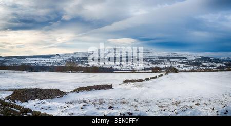Vue sur les champs enneigés et les murs de pierres sèches regardant vers une colline enneigée d'Addleborough sous un ciel nuageux Banque D'Images