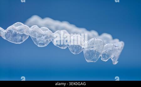 Macro gros plan d'un aligneur orthodontique transparent avec un second aligneur flou en arrière-plan sur un fond clinique bleu. Banque D'Images