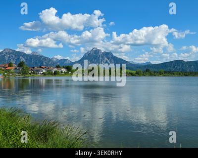 Allemagne, Lakeshore à Hopfen am See avec des maisons de village et des montagnes alpines enneigées Banque D'Images