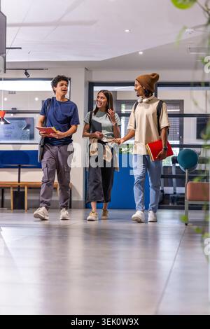 Étudiants divers marchant et parlant dans le hall moderne du campus tenant des cahiers et des sacs à dos Banque D'Images