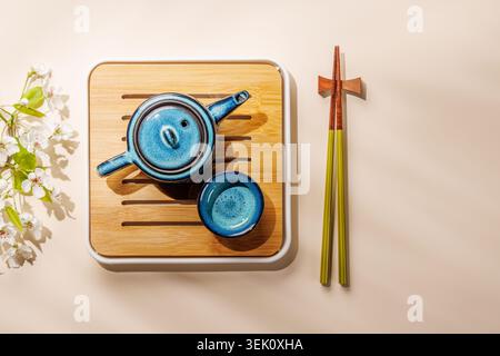 Théière en céramique bleue avec branche de printemps fleurie sur plateau en bois dans une composition minimale de style asiatique Banque D'Images