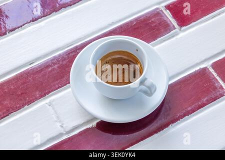 Plan en grand angle d'une tasse de café expresso italienne classique servie sur une table en bois peint rustique et vibrante sur une charmante terrasse de café en plein air en Italie. Banque D'Images