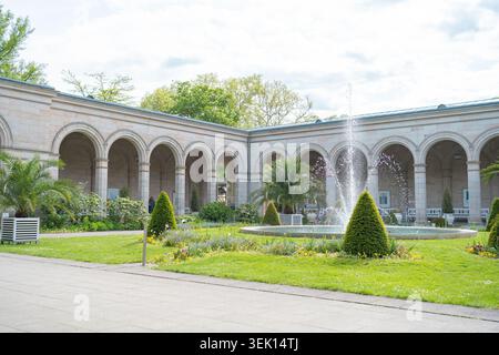 Une vue pittoresque sur un jardin public verdoyant avec une fontaine d'eau tirée à travers une majestueuse arcade en pierre voûtée à colonnade. Beau classique Banque D'Images