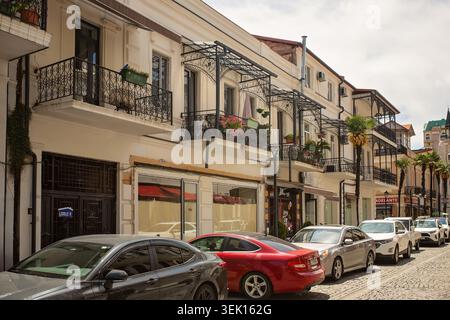 Batumi, Géorgie - 23 mai 2026 : rue historique avec des maisons traditionnelles, des balcons ornés, des boutiques et des voitures garées sur un trottoir pavé. Banque D'Images