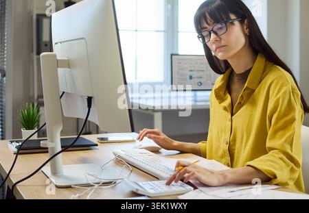 Femme focalisée faisant la budgétisation financière à l'ordinateur avec calculatrice dans le bureau moderne Banque D'Images