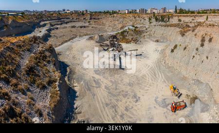 La perspective aérienne capture une carrière animée à ciel ouvert à Bichkek, au Kirghizistan. L'extraction industrielle est équipée d'un chargeur frontal jaune et d'un système de décharge orange tr Banque D'Images