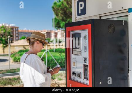 Femme payant au parcmètre dans la station balnéaire côtière Banque D'Images