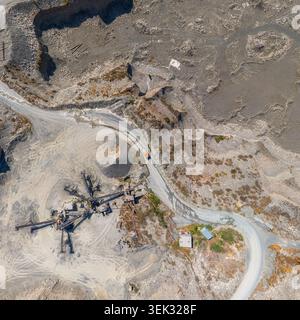 La vue aérienne capture un vaste site industriel de carrière au Kirghizistan. Les chemins de terre sinueux et les machines industrielles mettent en valeur les terrains accidentés et l'activité. Banque D'Images