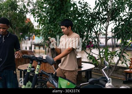Jeune homme louant scooter de mobilité électrique partagé en utilisant l'application smartphone Banque D'Images