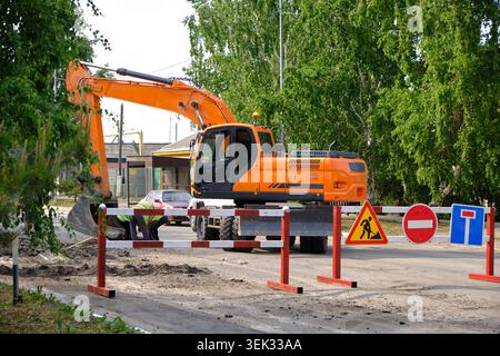 Grande pelle orange travaillant sur la réparation des rues derrière les panneaux de signalisation et les barrières le jour ensoleillé Banque D'Images