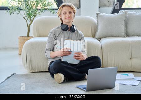 Jeune étudiant masculin souriant étudiant avec un ordinateur portable sur le sol à la maison Banque D'Images