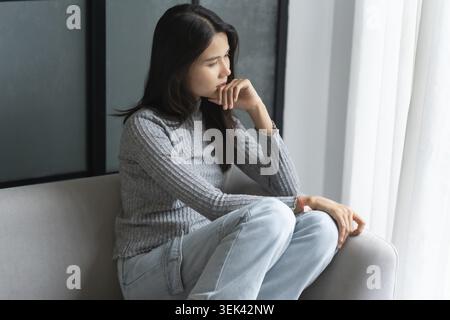 Jeune femme asiatique se sent seule, triste, malade, stressée, seule à la maison sur le canapé pour profiter du mode de vie de bien-être dans les soins de santé Banque D'Images