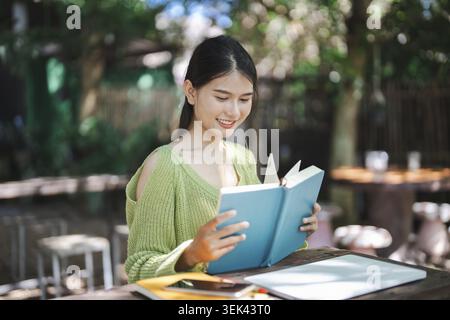 Belle jeune femme asiatique lisant livre, éducation ou étudiant sur le campus, portrait, bonheur en plein air dans le parc universitaire Banque D'Images