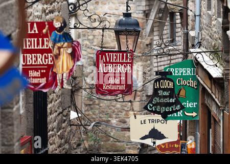 Panneaux d'hôtel et de restaurant suspendus dans une rue étroite au Mont Saint-Michel, Normandie, France. Banque D'Images