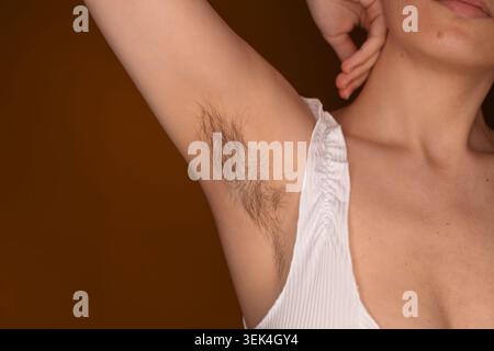 Gros plan d'une femme avec des poils naturels aux aisselles et le bras levé sur fond de studio orange, poils féminins, texture naturelle de la peau, positivité du corps Banque D'Images